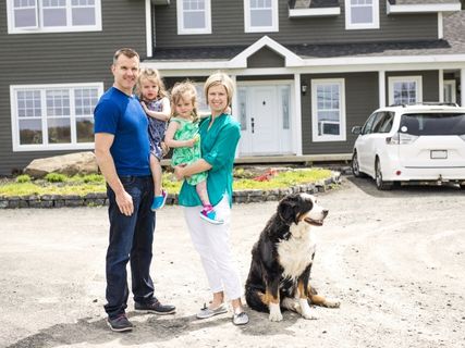 family smiling with their house behind them